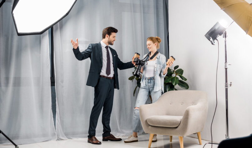 happy businessman holding coffee to go and talking with photographer in studio